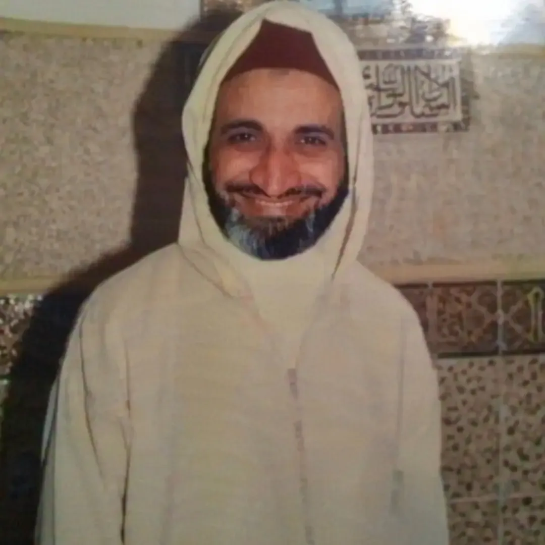 فريد الأنصاري مبتسمًا بجلباب أبيض أمام جدارٍ من الزليج