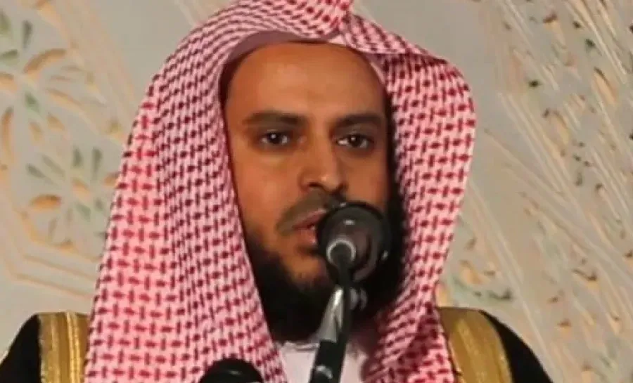 الشيخ عبد العزيز الطريفي بالشماغ الأحمر والبشت، يتكلّم أمام مكبّر صوت، وخلفه جدار منقوش