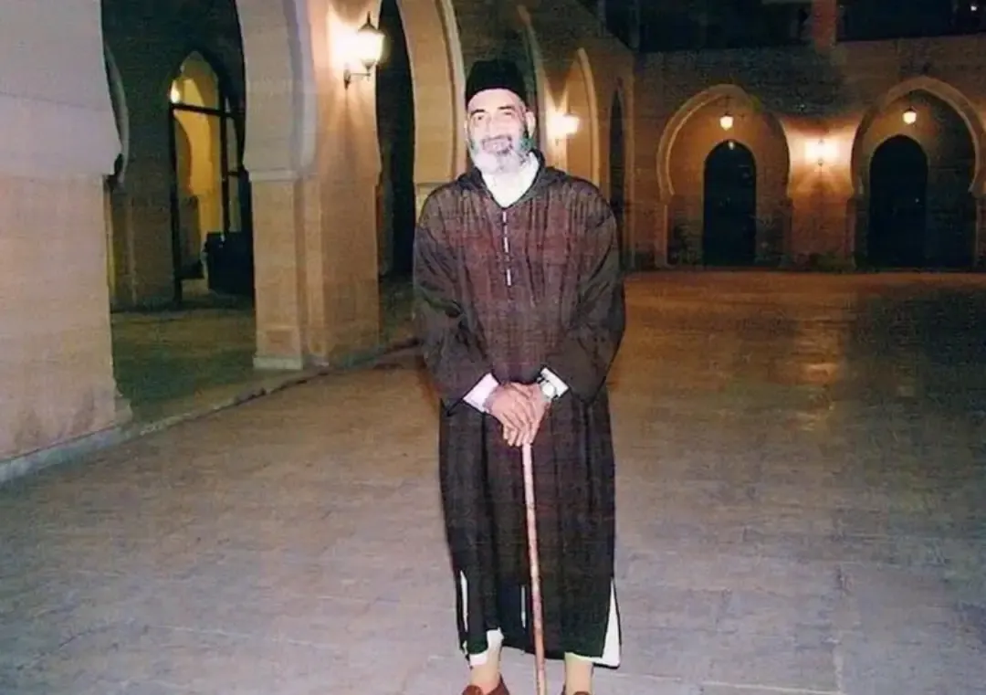 فريد الأنصاري متوكئًا على عصا في رواقٍ مضاء ليلًا