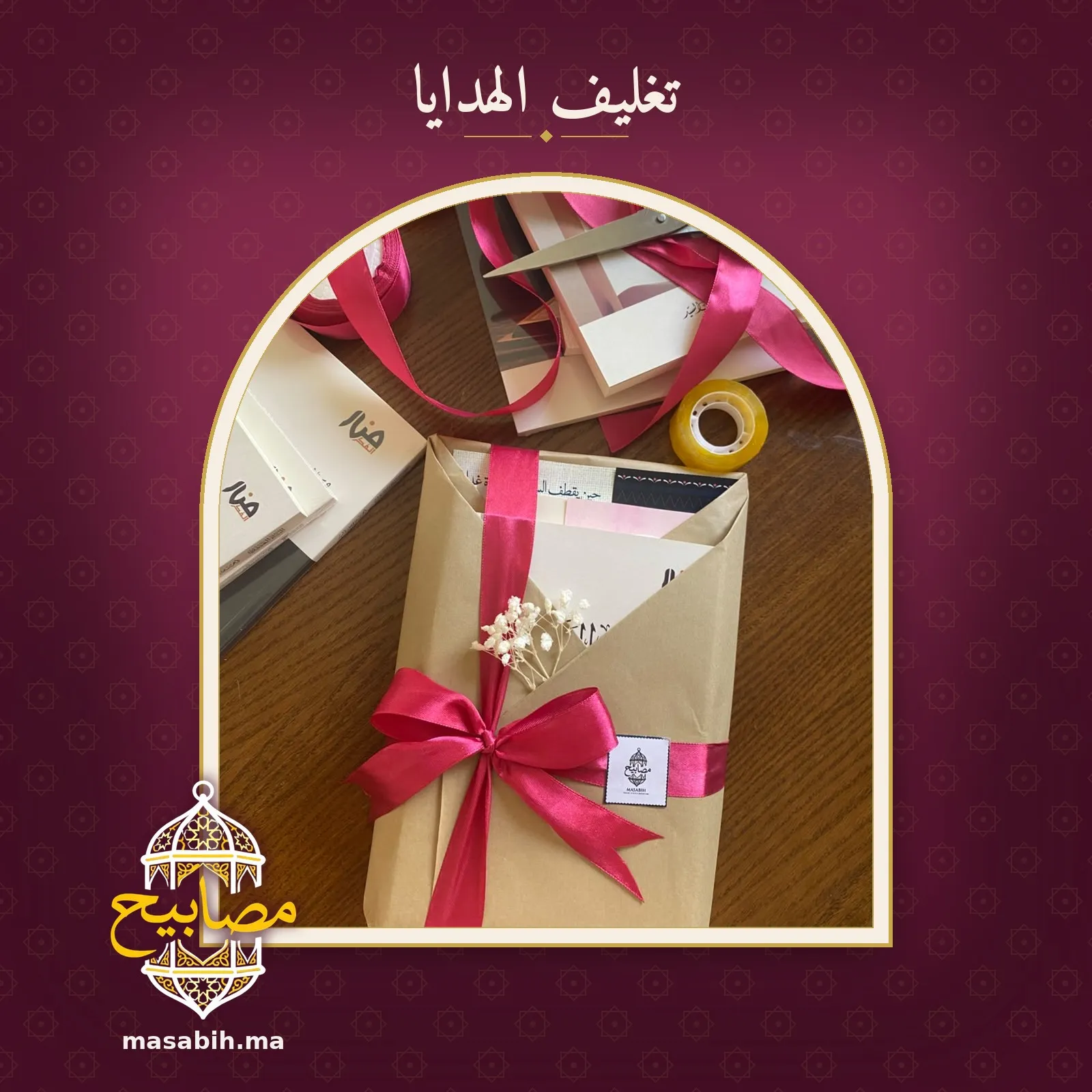هديةٌ على طاولة التغليف: كتبٌ في ورقٍ مطويّ يشدّه شريطٌ أحمر معقود، وغصنُ زهرٍ أبيض، وحولها مقصٌّ وبكرةُ شريطٍ لاصق ولفّةُ شريط